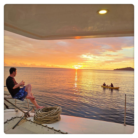 Person sitting on a Party Boat Kota Kinabalu deck watching a sunset over water with another boat in the distance.