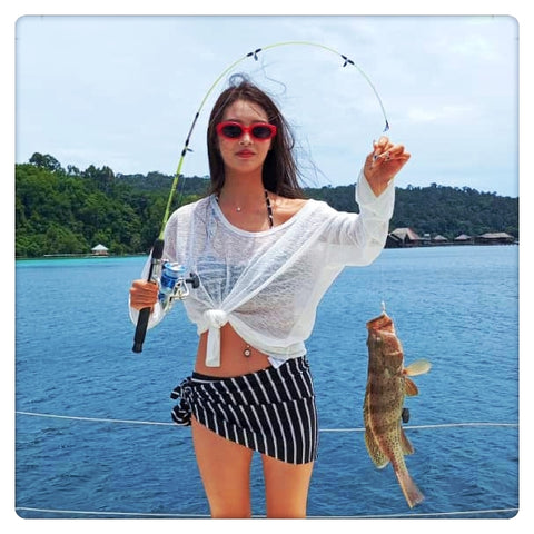 Woman holding a fishing rod with a fish caught, standing on a Party Boat Kota Kinabalu with a scenic background.