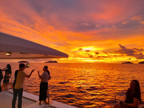People on a Party Boat Kota Kinabalu at sunset with vibrant orange and purple sky.