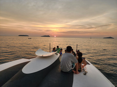 Guests relaxing on the Snowy Yacht during a stunning sunset cruise off the coast of Kota Kinabalu, with islands visible on the horizon.
