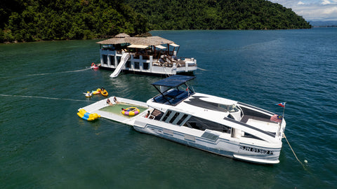 Snowy Yacht anchored beside the Floating Club House in Kota Kinabalu, featuring a floating pool and colorful inflatables for guests enjoying water activities.