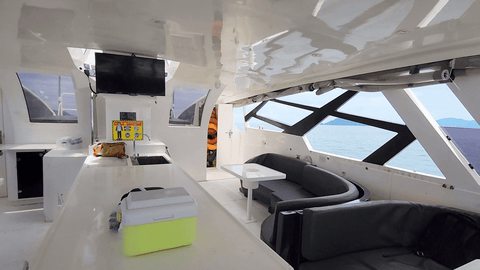 Spacious interior of the Snowy Yacht featuring a lounge area, TV, and mini bar setup with wide sea views through panoramic windows in Kota Kinabalu.