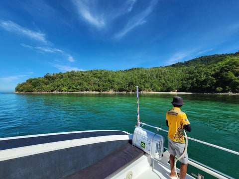 Crew member standing at the front deck of the Snowy Yacht near Gaya Island, Kota Kinabalu, surrounded by clear turquoise water and lush tropical forest.