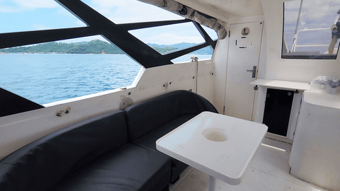Interior view of the Snowy Yacht in Kota Kinabalu, featuring a cozy seating area with a table and ocean view through large windows.